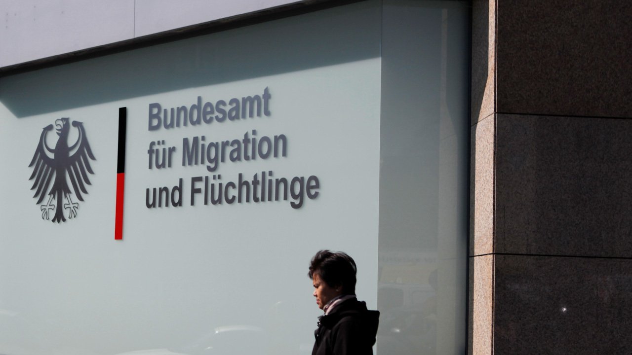 in the background there is the building of the bundesamt für migration und flüchtlinge. a person is walking infront of the building.