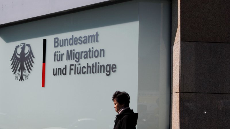 in the background there is the building of the bundesamt für migration und flüchtlinge. a person is walking infront of the building.