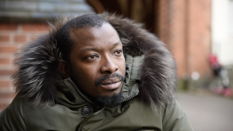 Black man in green parker looking pensive